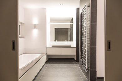 На фото: большая ванная комната в современном стиле с плоскими фасадами, белыми фасадами, накладной ванной, серой плиткой, белыми стенами и настольной раковиной