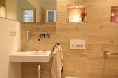 Inredning av ett modernt stort en-suite badrum, med öppna hyllor, vita skåp, ett platsbyggt badkar, en kantlös dusch, en vägghängd toalettstol, travertinkakel, vita väggar, klinkergolv i småsten, ett väggmonterat handfat, flerfärgat golv och med dusch som är öppen