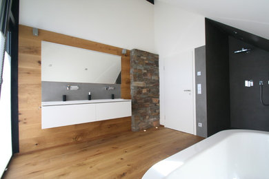 Photo of a large contemporary ensuite bathroom in Cologne with flat-panel cabinets, white cabinets, a freestanding bath, a built-in shower, a wall mounted toilet, white tiles, stone slabs, white walls, dark hardwood flooring, an integrated sink, wooden worktops, brown floors and an open shower.