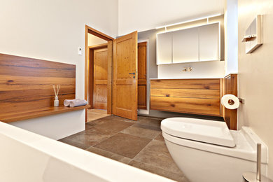 Mittelgroßes Modernes Badezimmer mit flächenbündigen Schrankfronten, hellbraunen Holzschränken, Wandtoilette mit Spülkasten, weißer Wandfarbe und braunem Boden in München