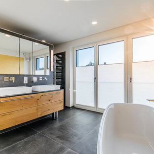 Modernes Badezimmer En Suite mit flächenbündigen Schrankfronten, hellbraunen Holzschränken, freistehender Badewanne, weißer Wandfarbe, Aufsatzwaschbecken, grauem Boden und schwarzer Waschtischplatte in Nürnberg