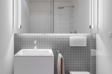 Kleines Modernes Badezimmer mit flächenbündigen Schrankfronten, weißen Schränken, Eckdusche, Wandtoilette, grauen Fliesen, Keramikfliesen, weißer Wandfarbe und integriertem Waschbecken in Hamburg