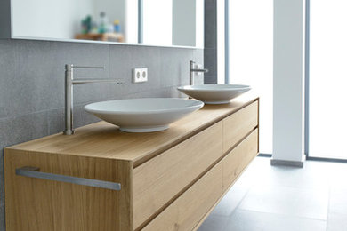 Modernes Badezimmer mit hellbraunen Holzschränken, grauen Fliesen und Waschtisch aus Holz in Dortmund