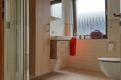 Mittelgroßes Badezimmer mit hellen Holzschränken, bodengleicher Dusche, Wandtoilette, Keramikfliesen, Aufsatzwaschbecken, Mineralwerkstoff-Waschtisch und Falttür-Duschabtrennung