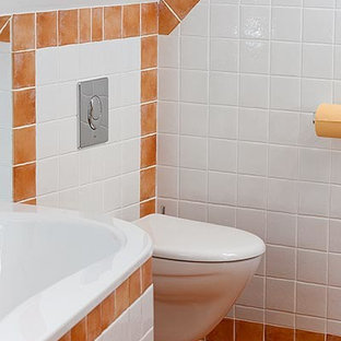 Mittelgroßes Klassisches Duschbad mit profilierten Schrankfronten, weißen Schränken, Eckbadewanne, Eckdusche, Wandtoilette, farbigen Fliesen, Keramikfliesen, weißer Wandfarbe, Terrakottaboden, Einbauwaschbecken, Mineralwerkstoff-Waschtisch, orangem Boden und Falttür-Duschabtrennung in Hamburg