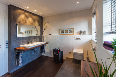 Ejemplo de cuarto de baño actual grande con sanitario de pared, paredes grises, suelo de madera oscura, lavabo sobreencimera, encimera de madera y suelo marrón