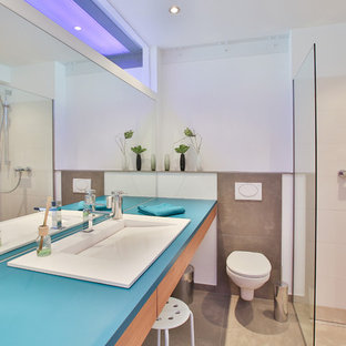 Kleines Industrial Duschbad mit flächenbündigen Schrankfronten, hellen Holzschränken, braunen Fliesen, weißer Wandfarbe, Einbauwaschbecken, beigem Boden, offener Dusche, blauer Waschtischplatte, Eckdusche und Wandtoilette in Köln
