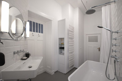Idéer för ett litet modernt badrum, med släta luckor, vita skåp, ett fristående badkar, en dusch/badkar-kombination, en vägghängd toalettstol, vit kakel, keramikplattor, vita väggar, ett väggmonterat handfat, grått golv och dusch med duschdraperi