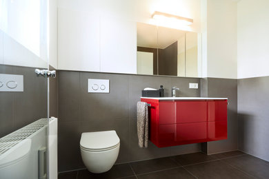 Kleines Modernes Duschbad mit flächenbündigen Schrankfronten, roten Schränken, bodengleicher Dusche, Wandtoilette mit Spülkasten, grauen Fliesen, weißer Wandfarbe, Einbauwaschbecken, grauem Boden und weißer Waschtischplatte in Stuttgart