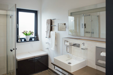 Idéer för att renovera ett stort funkis en-suite badrum, med släta luckor, vita skåp, ett platsbyggt badkar, en kantlös dusch, en vägghängd toalettstol, vit kakel, porslinskakel, vita väggar, klinkergolv i porslin, ett fristående handfat, träbänkskiva, svart golv och med dusch som är öppen