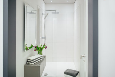 Modern inredning av ett mellanstort badrum med dusch, med släta luckor, grå skåp, en kantlös dusch, en vägghängd toalettstol, vit kakel, porslinskakel, vita väggar, klinkergolv i porslin, ett fristående handfat, träbänkskiva, grått golv och med dusch som är öppen