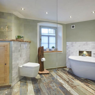 Großes Rustikales Badezimmer En Suite mit freistehender Badewanne, offener Dusche, Wandtoilette, grauen Fliesen, grüner Wandfarbe, gebeiztem Holzboden, buntem Boden und offener Dusche in Sonstige