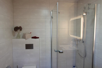 Foto de cuarto de baño contemporáneo de tamaño medio con ducha esquinera, sanitario de pared, paredes blancas, aseo y ducha, suelo gris y ducha con puerta con bisagras