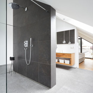 Modernes Badezimmer En Suite mit offenen Schränken, hellen Holzschränken, bodengleicher Dusche, schwarzen Fliesen, weißer Wandfarbe, grauem Boden, offener Dusche, schwebendem Waschtisch und gewölbter Decke in München