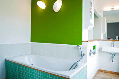Großes Modernes Badezimmer mit Einbaubadewanne, weißen Fliesen, grüner Wandfarbe, braunem Holzboden und Wandwaschbecken in Dortmund