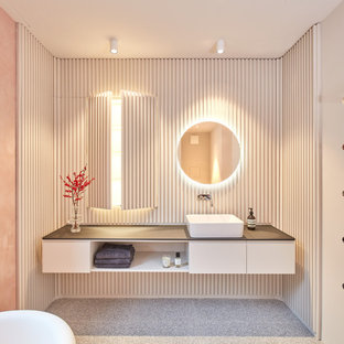Inredning av ett modernt stort svart svart badrum med dusch, med luckor med lamellpanel, vita skåp, ett fristående badkar, en kantlös dusch, en vägghängd toalettstol, rosa väggar, terrazzogolv, ett fristående handfat, träbänkskiva, grått golv och med dusch som är öppen
