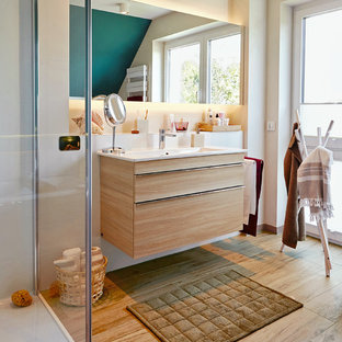 Mittelgroßes Maritimes Duschbad mit flächenbündigen Schrankfronten, weißer Wandfarbe, hellen Holzschränken, integriertem Waschbecken, beigem Boden, weißer Waschtischplatte, Duschnische, weißen Fliesen, braunem Holzboden und Falttür-Duschabtrennung in Sonstige