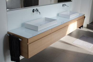 Imagen de cuarto de baño contemporáneo con armarios con paneles lisos, puertas de armario de madera clara, paredes blancas, encimera de madera, suelo gris y encimeras blancas