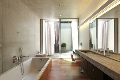 Immagine di una stanza da bagno contemporanea di medie dimensioni con ante lisce, ante nere, vasca da incasso, bidè, pareti grigie, pavimento in legno massello medio e lavabo integrato