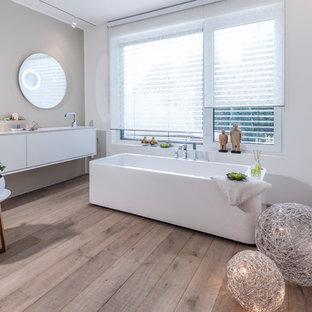 Großes Modernes Duschbad mit flächenbündigen Schrankfronten, weißen Schränken, freistehender Badewanne, weißer Wandfarbe, gebeiztem Holzboden, integriertem Waschbecken und braunem Boden in Düsseldorf