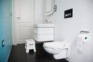 Photo of a small contemporary family bathroom in Cologne with flat-panel cabinets, white cabinets, a wall mounted toilet, cement flooring, a built-in sink and black floors.