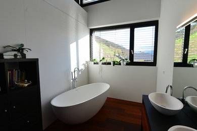 Modernes Badezimmer mit freistehender Badewanne, weißer Wandfarbe, Waschtisch aus Holz und weißen Fliesen