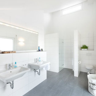 Großes Nordisches Duschbad mit weißen Fliesen, weißer Wandfarbe, Wandwaschbecken, grauem Boden, Falttür-Duschabtrennung, bodengleicher Dusche, Wandtoilette mit Spülkasten und Keramikboden in Stuttgart