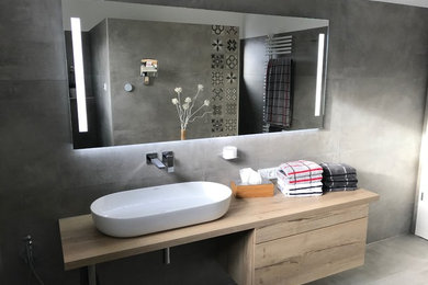 Modernes Badezimmer mit flächenbündigen Schrankfronten, hellen Holzschränken, grauen Fliesen, Aufsatzwaschbecken und Waschtisch aus Holz in Köln