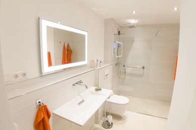 Modernes Duschbad mit bodengleicher Dusche, Wandtoilette mit Spülkasten, weißen Fliesen, beigem Boden, offener Dusche, Wäscheaufbewahrung, Einzelwaschbecken und schwebendem Waschtisch in Sonstige