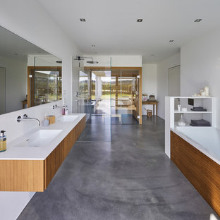 Modernes Badezimmer En Suite mit flächenbündigen Schrankfronten, hellbraunen Holzschränken, Einbaubadewanne, bodengleicher Dusche, weißen Fliesen, weißer Wandfarbe, Betonboden, integriertem Waschbecken, grauem Boden, offener Dusche und weißer Waschtischplatte in Dortmund