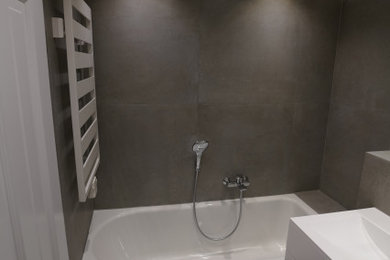 Inspiration för mellanstora moderna vitt badrum, med släta luckor, vita skåp, ett badkar i en alkov, en vägghängd toalettstol, grå kakel, vita väggar, ett integrerad handfat, bänkskiva i akrylsten, grått golv och stenkakel