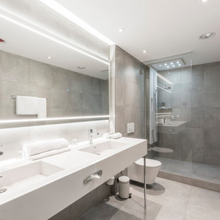 Großes Modernes Duschbad mit offenen Schränken, Duschnische, Wandtoilette, grauen Fliesen, Porzellanfliesen, Porzellan-Bodenfliesen, integriertem Waschbecken, grauem Boden und weißer Waschtischplatte in Frankfurt am Main