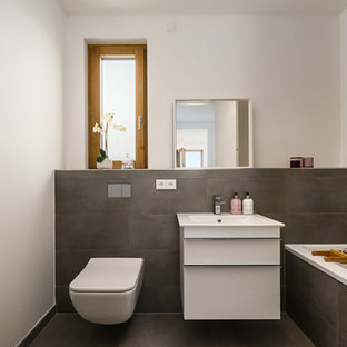Kleines Modernes Duschbad mit flächenbündigen Schrankfronten, weißen Schränken, Einbaubadewanne, Wandtoilette, grauen Fliesen, Zementfliesen, weißer Wandfarbe, Waschtischkonsole und grauem Boden in München