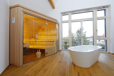 Modelo de sauna contemporánea de tamaño medio con bañera exenta, paredes blancas, suelo de madera clara y suelo beige