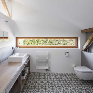 Country Badezimmer mit offenen Schränken, hellbraunen Holzschränken, Wandtoilette, grauen Fliesen, weißer Wandfarbe, Zementfliesen, Aufsatzwaschbecken, Waschtisch aus Holz, buntem Boden und brauner Waschtischplatte in München