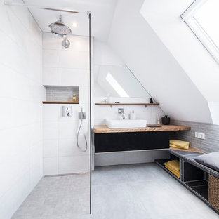 Cette photo montre une salle d'eau tendance de taille moyenne avec une vasque, un carrelage gris, des carreaux de céramique, un mur blanc, un sol en carrelage de céramique, des portes de placard noires, une douche ouverte, un plan de toilette en bois et aucune cabine.