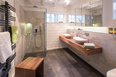 Ejemplo de cuarto de baño contemporáneo de tamaño medio con ducha a ras de suelo, baldosas y/o azulejos grises, paredes blancas, lavabo sobreencimera, encimera de madera y suelo gris