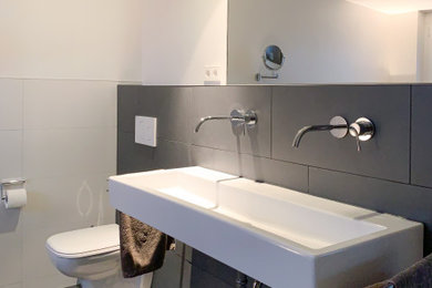 Mittelgroßes Modernes Badezimmer mit Wandtoilette mit Spülkasten, grauen Fliesen, Keramikfliesen, weißer Wandfarbe, Keramikboden, Trogwaschbecken und grauem Boden in Sonstige