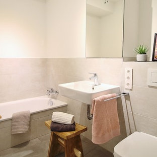 Kleines Nordisches Duschbad mit offenen Schränken, Badewanne in Nische, Wandtoilette, grauen Fliesen, beiger Wandfarbe, Wandwaschbecken, grauem Boden, Zementfliesen und Zementfliesen in Hamburg