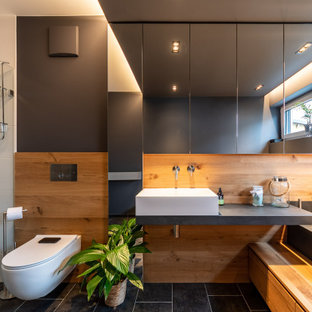Mittelgroßes Modernes Duschbad mit Wandtoilette, braunen Fliesen, Porzellanfliesen, schwarzer Wandfarbe, Porzellan-Bodenfliesen, Aufsatzwaschbecken, schwarzem Boden, grauer Waschtischplatte, Einzelwaschbecken und schwebendem Waschtisch in München