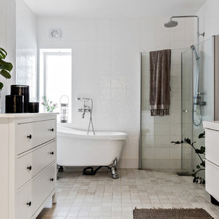 Minimalistisk inredning av ett en-suite badrum, med släta luckor, vita skåp, ett badkar med tassar, en hörndusch, vit kakel, vita väggar, beiget golv och dusch med gångjärnsdörr