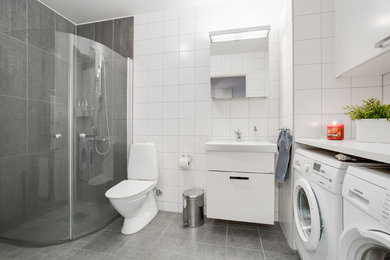 Modernes Badezimmer mit flächenbündigen Schrankfronten, weißen Schränken, Eckdusche, Toilette mit Aufsatzspülkasten, weißen Fliesen, Zementfliesen für Boden, Wandwaschbecken und Laminat-Waschtisch in Göteborg