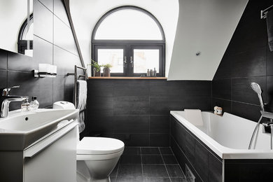 Modern inredning av ett stort badrum, med släta luckor, vita skåp, ett undermonterat badkar, en dusch/badkar-kombination, en toalettstol med hel cisternkåpa, keramikplattor, svarta väggar, kalkstensgolv, ett integrerad handfat, svart kakel och svart golv