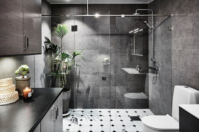 Modern inredning av ett mellanstort badrum med dusch, med släta luckor, skåp i mellenmörkt trä, en toalettstol med hel cisternkåpa, grå kakel, keramikplattor, klinkergolv i keramik, ett avlångt handfat, laminatbänkskiva, en dusch i en alkov, grå väggar, vitt golv och dusch med gångjärnsdörr