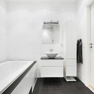 Idéer för att renovera ett mellanstort nordiskt svart svart badrum, med släta luckor, vita skåp, ett platsbyggt badkar, vit kakel, vita väggar, ett fristående handfat och svart golv