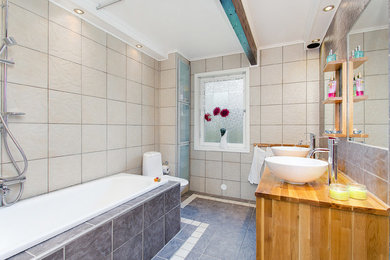 Modern inredning av ett badrum med dusch, med skåp i mellenmörkt trä, ett platsbyggt badkar, en dusch/badkar-kombination, en toalettstol med hel cisternkåpa, beige kakel, keramikplattor, beige väggar, klinkergolv i keramik och ett fristående handfat