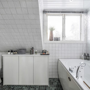 Bild på ett minimalistiskt vit vitt badrum, med vita skåp, ett hörnbadkar, en dusch/badkar-kombination, en toalettstol med hel cisternkåpa, vit kakel, vita väggar, grönt golv och med dusch som är öppen