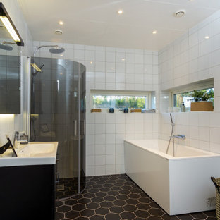 Modern inredning av ett mellanstort vit vitt badrum med dusch, med släta luckor, svarta skåp, ett hörnbadkar, en hörndusch, vit kakel, porslinskakel, klinkergolv i porslin, ett integrerad handfat, svart golv och dusch med gångjärnsdörr
