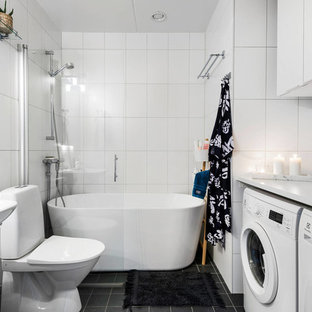 Bild på ett stort skandinaviskt vit vitt badrum, med släta luckor, vita skåp, ett fristående badkar, en kantlös dusch, vit kakel, vita väggar, ett konsol handfat, svart golv och med dusch som är öppen
