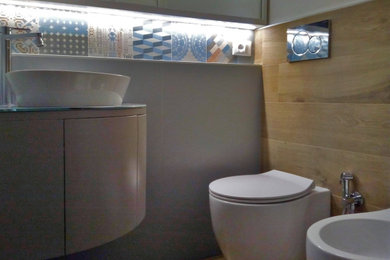 Modern inredning av ett litet toalett, med luckor med profilerade fronter, en toalettstol med separat cisternkåpa, flerfärgad kakel, porslinskakel, vita väggar, klinkergolv i porslin, ett fristående handfat och bänkskiva i glas